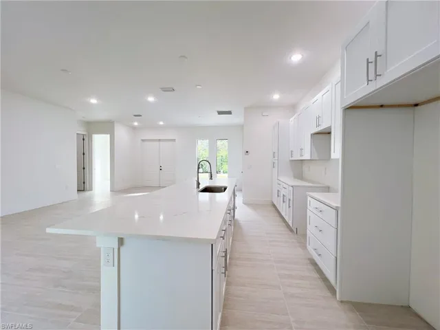 Kitchen with a kitchen island with sink, white cabinetry, sink, and light stone countertops