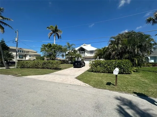 View of property hidden behind natural elements featuring a front lawn, decorative driveway, a garage, and a residential view