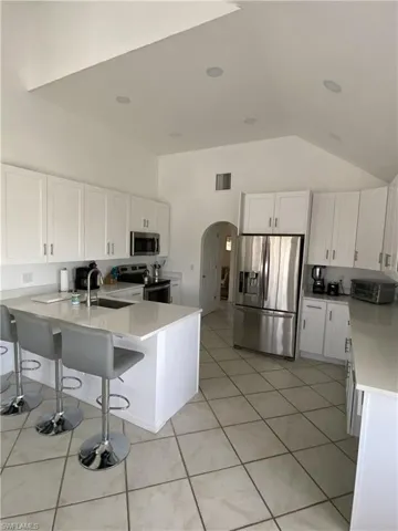 Kitchen featuring white cabinets, a breakfast bar, stainless steel appliances, a peninsula, and arched walkways
