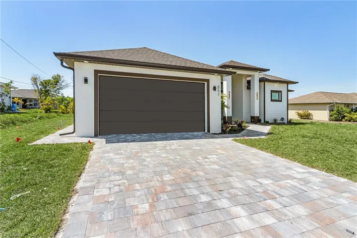 Prairie-style house with a front lawn, decorative driveway, stucco siding, and a garage