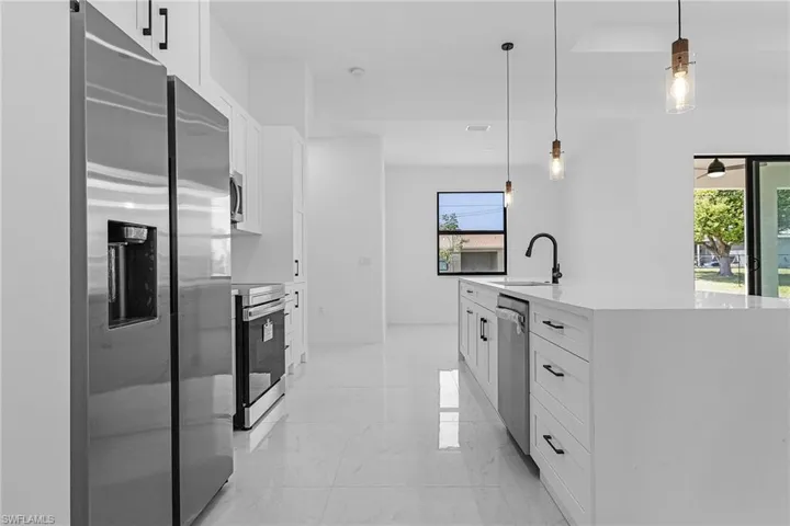 Kitchen with marble finish floor, a sink, pendant lighting, white cabinets, and appliances with stainless steel finishes
