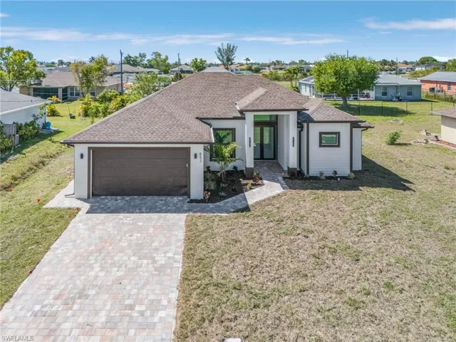 View of front of house featuring a shingled roof, decorative driveway, a front lawn, and an attached garage