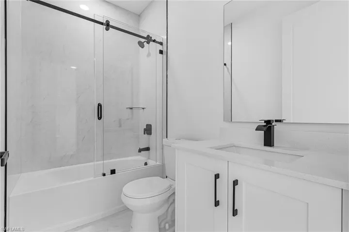 Full bath with marble finish floor, toilet, vanity, and bath / shower combo with glass door