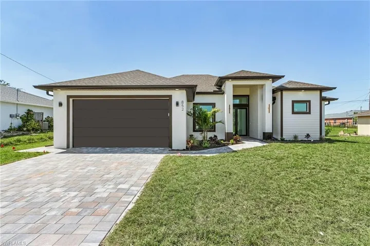 Prairie-style house with a front lawn, decorative driveway, a garage, and stucco siding