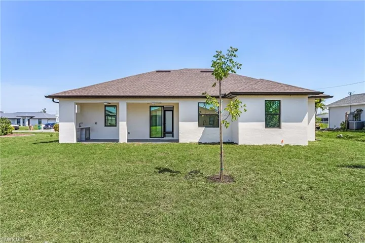 Rear view of house featuring a lawn, cooling unit, roof with shingles, and stucco siding