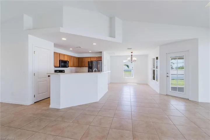 Kitchen with light tile patterned floors, black microwave, stainless steel refrigerator with ice dispenser, light countertops, and a notable chandelier