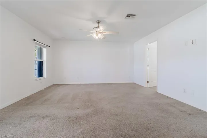 Spare room with carpet floors, ceiling fan, visible vents, and baseboards