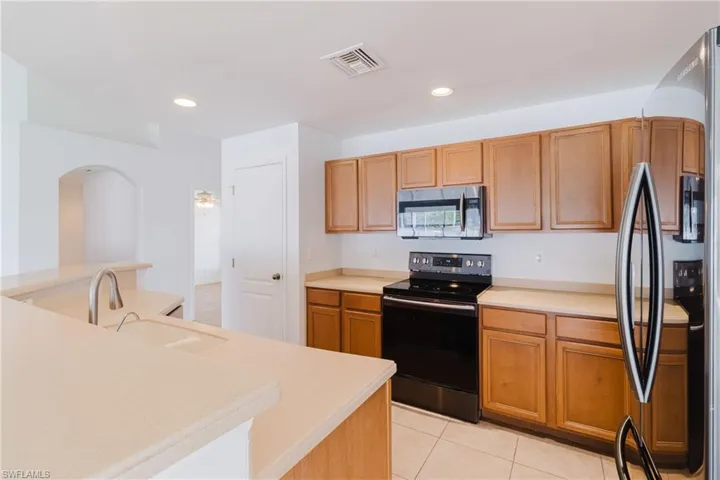 Kitchen with visible vents, freestanding refrigerator, black electric range oven, stainless steel microwave, and light tile patterned flooring