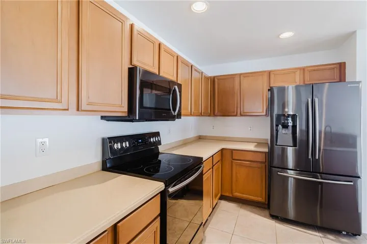 Kitchen featuring stainless steel fridge with ice dispenser, light tile patterned floors, recessed lighting, light countertops, and black / electric stove