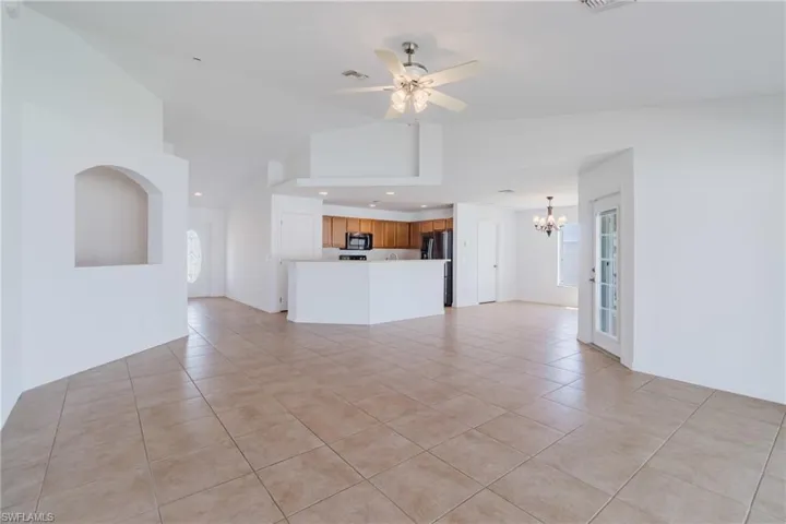 Unfurnished living room with light tile patterned floors, visible vents, ceiling fan with notable chandelier, and lofted ceiling