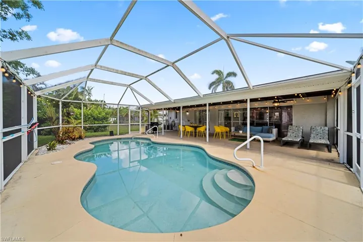 Screen-enclosed pool area featuring a freeform pool with integrated steps, a surrounding concrete deck, and a covered patio