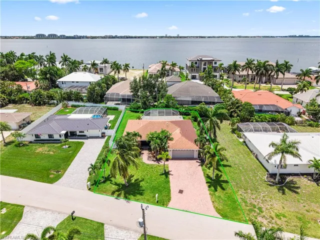 Aerial perspective showcasing a waterfront property with a red tile roof and a paver driveway