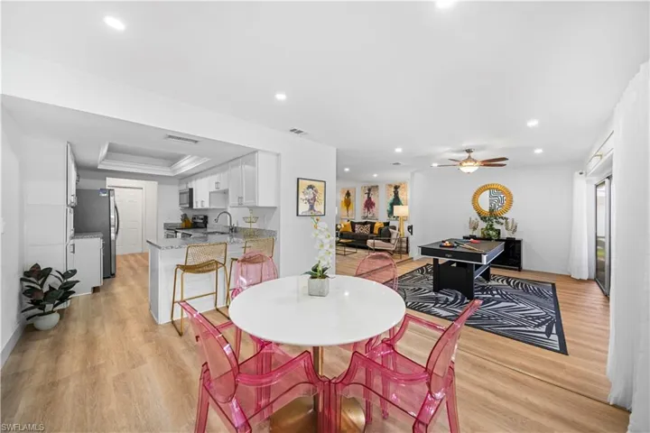 Open-concept living area with wood-finish flooring, recessed lighting, and a modern kitchen featuring white cabinetry and stainless steel appliances