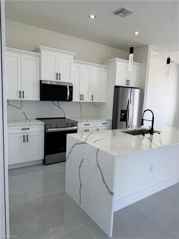 Modern kitchen featuring white shaker cabinetry with black hardware, stainless steel appliances, and sleek gray flooring