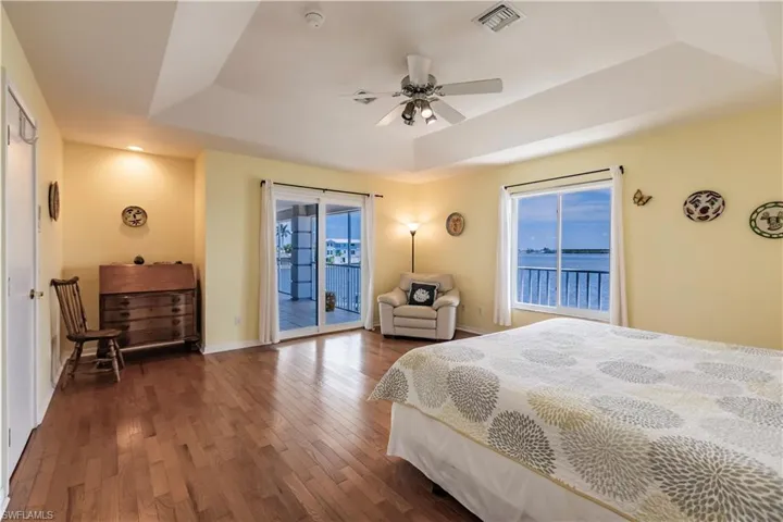 Bedroom with a tray ceiling, dark hardwood / wood-style floors, multiple windows, and ceiling fan