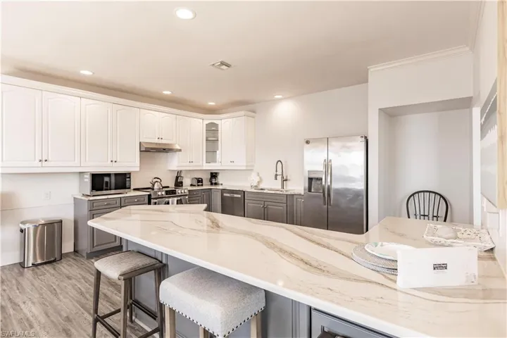 Kitchen featuring light stone countertops, light hardwood / wood-style floors, sink, white cabinets, and appliances with stainless steel finishes