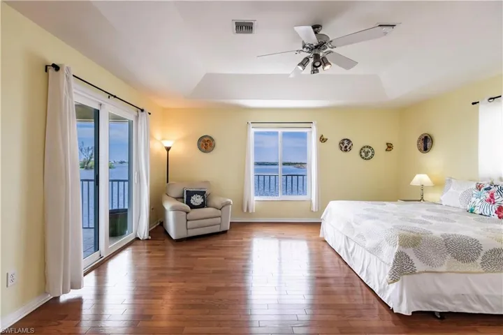 Bedroom with a raised ceiling, hardwood / wood-style floors, ceiling fan, and access to exterior