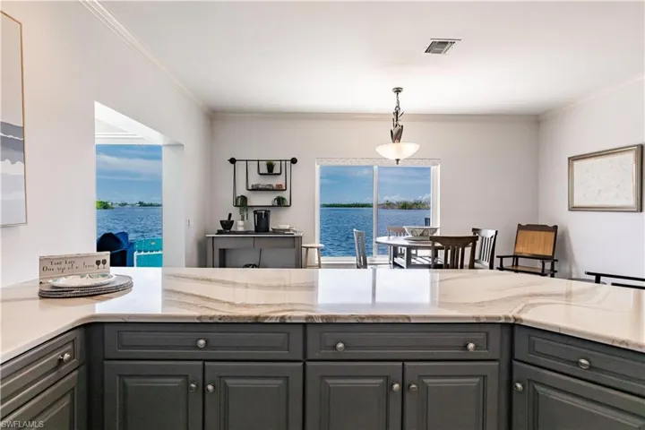 Kitchen with a water view, light stone countertops, crown molding, and pendant lighting