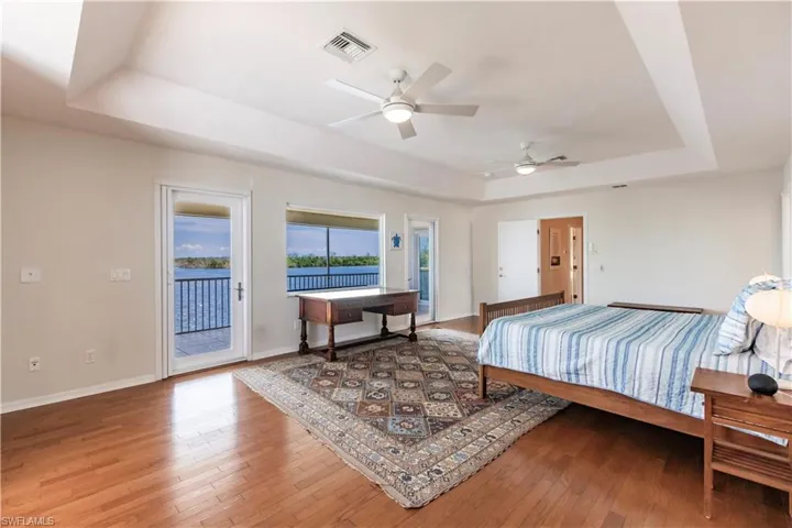 Bedroom with access to exterior, wood-type flooring, ceiling fan, and a raised ceiling