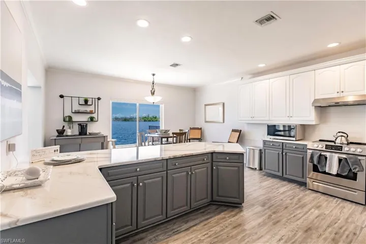 Kitchen featuring white cabinetry, light hardwood / wood-style floors, gray cabinetry, appliances with stainless steel finishes, and pendant lighting