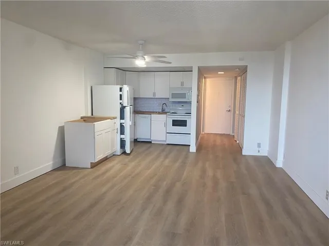 Kitchen with white cabinets, white appliances, light wood-type flooring, decorative backsplash, and a ceiling fan