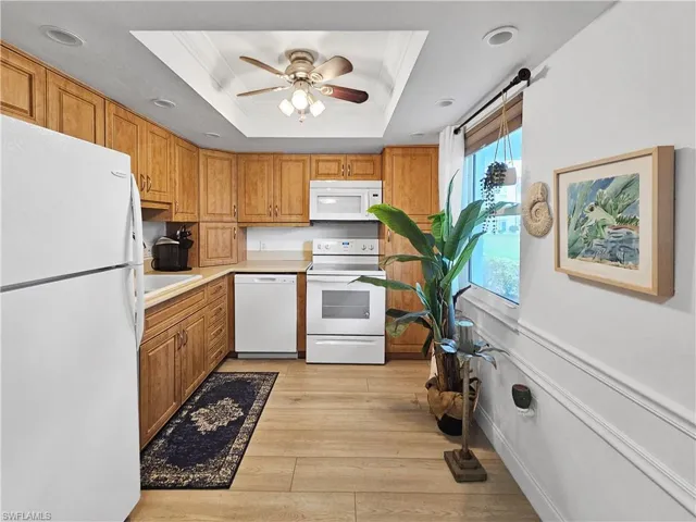 Kitchen featuring white appliances, a tray ceiling, light countertops, light wood-style flooring, and brown cabinetry
