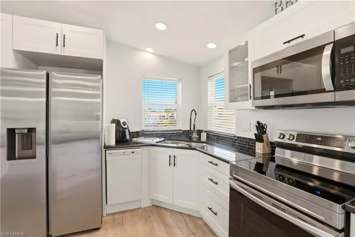 Kitchen featuring stainless steel appliances, white cabinetry, light wood finished floors, glass insert cabinets, and recessed lighting