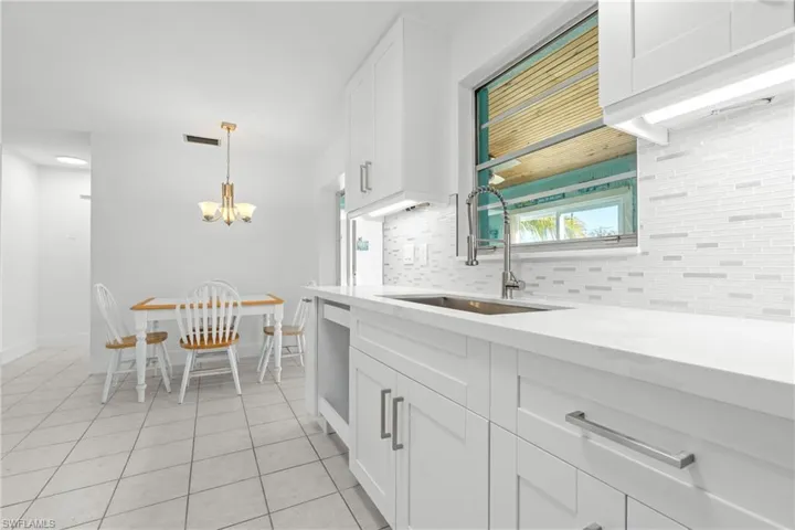 Kitchen with white cabinetry, decorative backsplash, a chandelier, hanging light fixtures, and light tile patterned flooring