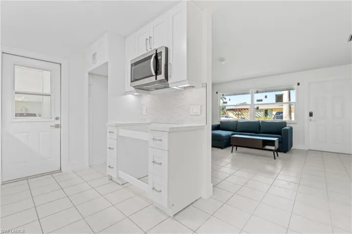 Kitchen featuring white cabinetry, light countertops, light tile patterned floors, stainless steel microwave, and backsplash