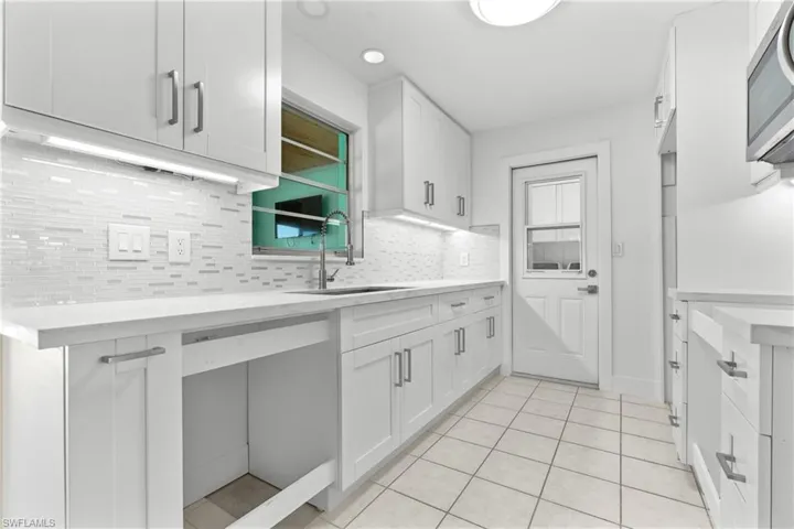 Kitchen featuring white cabinets, stainless steel microwave, backsplash, and light tile patterned floors