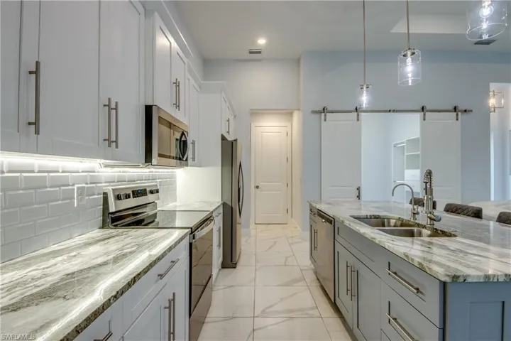 Kitchen featuring tasteful backsplash, a sink, appliances with stainless steel finishes, a kitchen island with sink, and marble finish floor