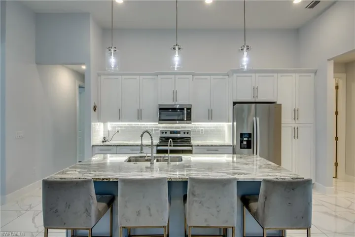 Kitchen featuring decorative backsplash, stainless steel appliances, marble finish floor, a sink, and baseboards