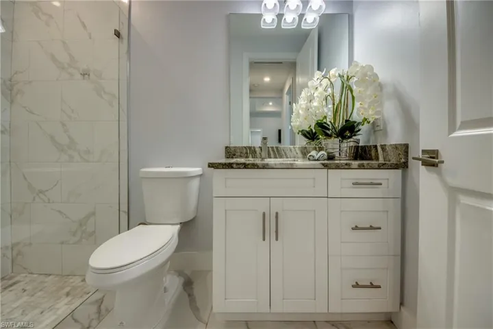 Full bathroom featuring vanity, toilet, a tile shower, marble finish floor, and baseboards