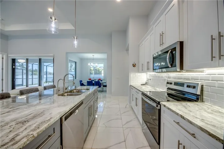 Kitchen featuring a sink, stainless steel appliances, tasteful backsplash, marble finish floor, and light stone counters