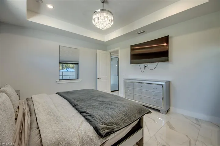 Bedroom with marble finish floor, baseboards, visible vents, a notable chandelier, and a tray ceiling