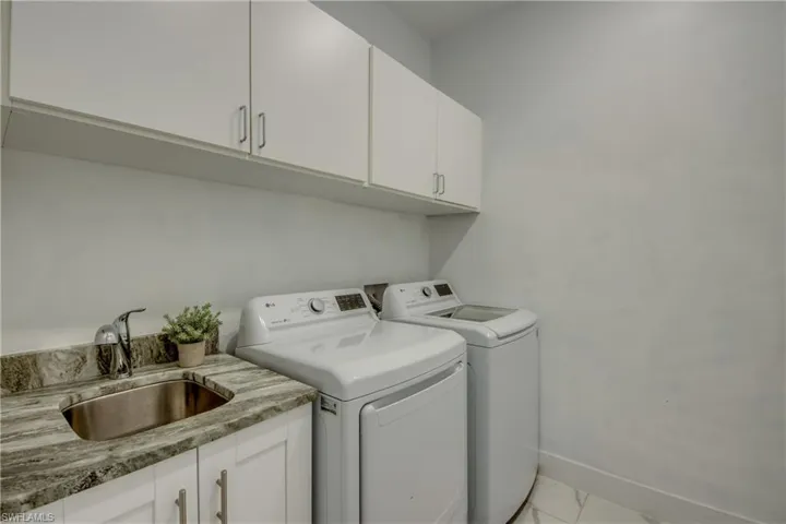 Washroom with a sink, cabinet space, independent washer and dryer, marble finish floor, and baseboards