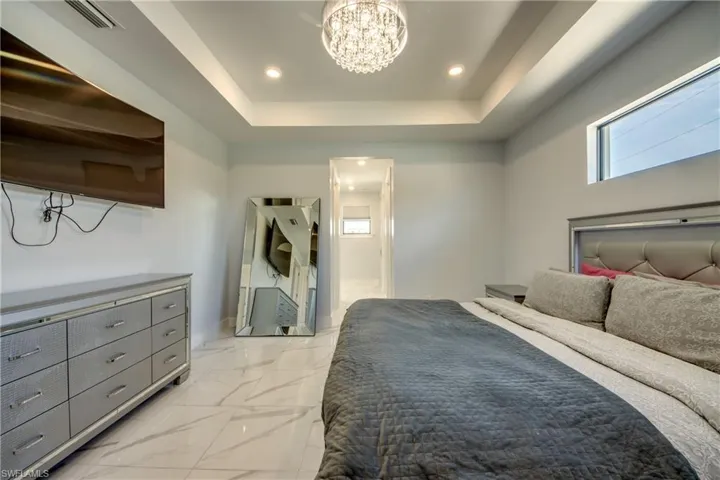 Bedroom featuring a chandelier, marble finish floor, baseboards, visible vents, and a tray ceiling