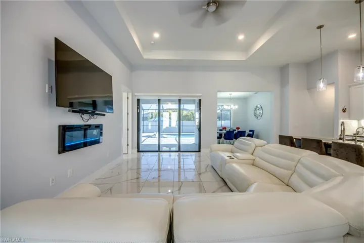 Living room with recessed lighting, marble finish floor, ceiling fan with notable chandelier, baseboards, and a raised ceiling