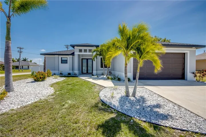 View of front facade with a front lawn, a garage, driveway, stucco siding, and french doors