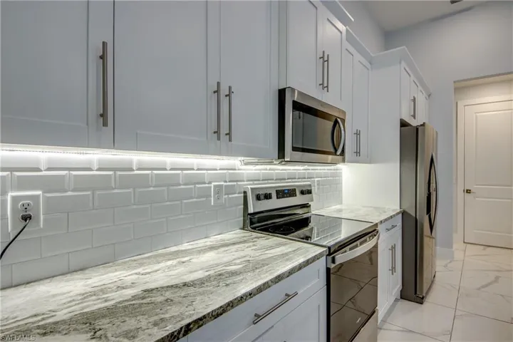 Kitchen featuring tasteful backsplash, light stone counters, appliances with stainless steel finishes, marble finish floor, and white cabinetry
