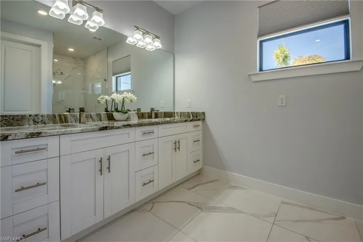 Full bathroom featuring a sink, a marble finish shower, double vanity, marble finish floor, and baseboards
