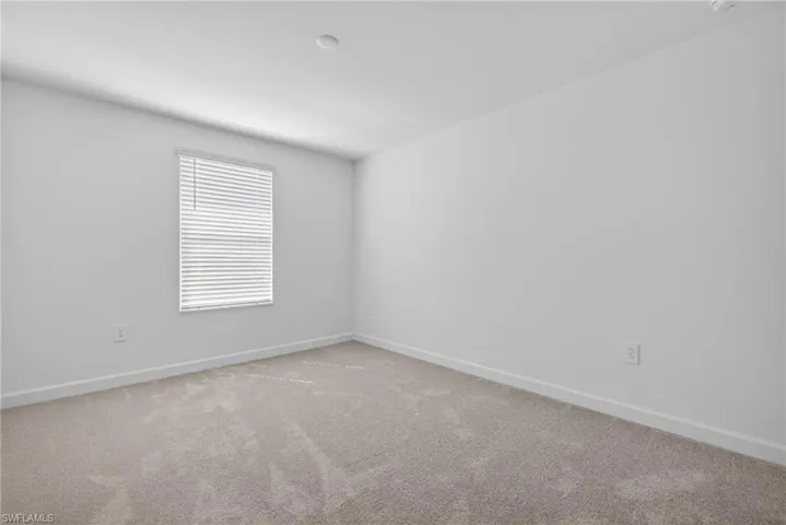 The property features an interior room with white walls, a window with blinds, and light-colored carpet