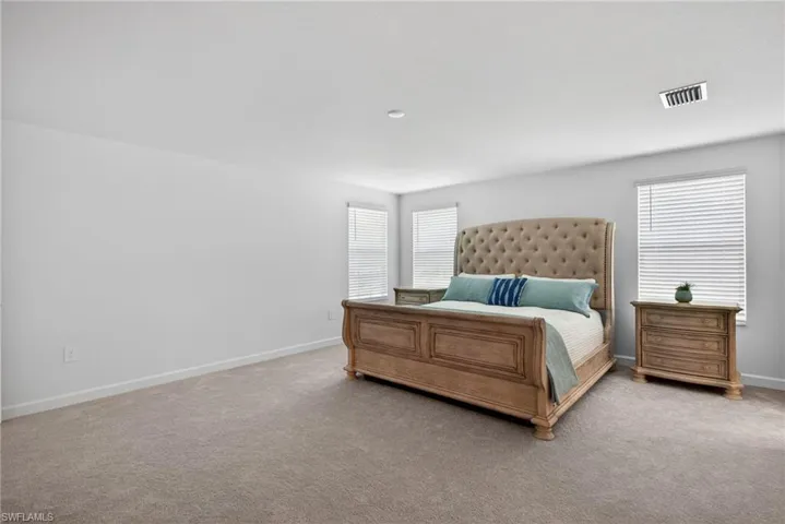 The room features light-colored carpeting, white walls, and multiple windows with blinds