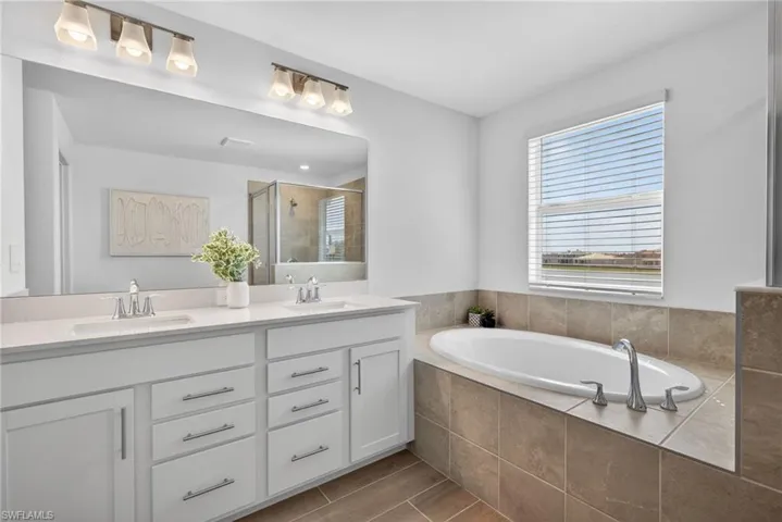 The bathroom features a dual vanity with white cabinetry and chrome hardware, a large mirror, and an oval-shaped bathtub surrounded by neutral-toned tiles