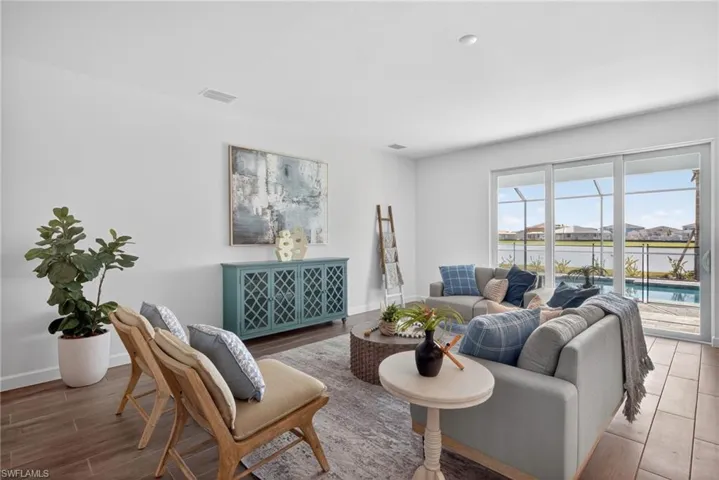 The living area features white walls, tile flooring, and sliding glass doors that open to a screened lanai with a pool and water views
