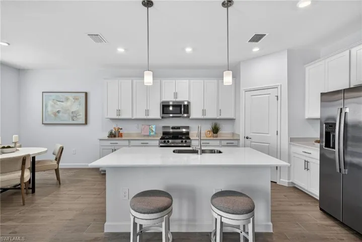 The kitchen features white cabinetry, stainless steel appliances, and a central island with a sink and pendant lighting