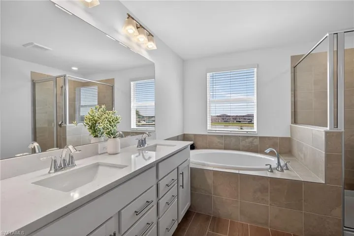 Bathroom featuring a double vanity with light-colored countertops, a large mirror, a built-in bathtub with tiled surround, and a walk-in shower with glass enclosure