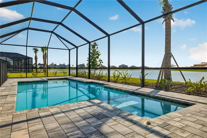Screened-in swimming pool with a paved deck, offering open views of a body of water and surrounding landscaping