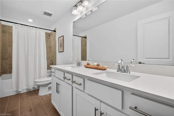 Bathroom featuring a double vanity with white cabinetry and a light-colored countertop, along with a bathtub and shower combination with tan tiled walls
