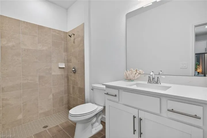 Bathroom featuring a tiled shower with a shower head and control, a toilet, and a vanity with an integrated sink and chrome faucet